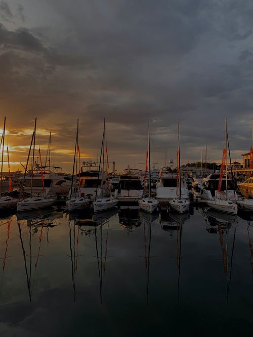Free Captivating view of sailboats in a harbor reflecting on water during sunset. Stock Photo