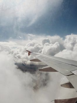 Breathtaking view of an airplane wing flying through fluffy clouds in a blue sky.