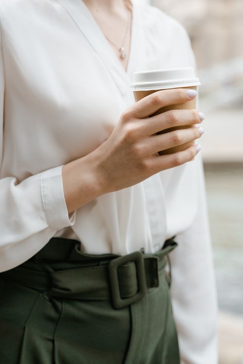 Free Close-up of a woman holding a coffee cup, dressed in elegant attire, enjoying outdoors. Stock Photo