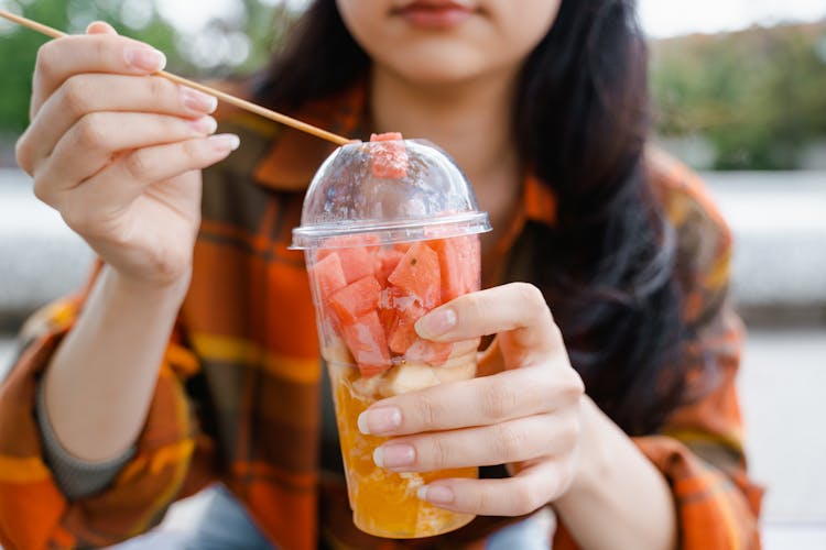 
A Close-Up Shot Of A Woman Eating Sliced Fruit In A Plastic Cup