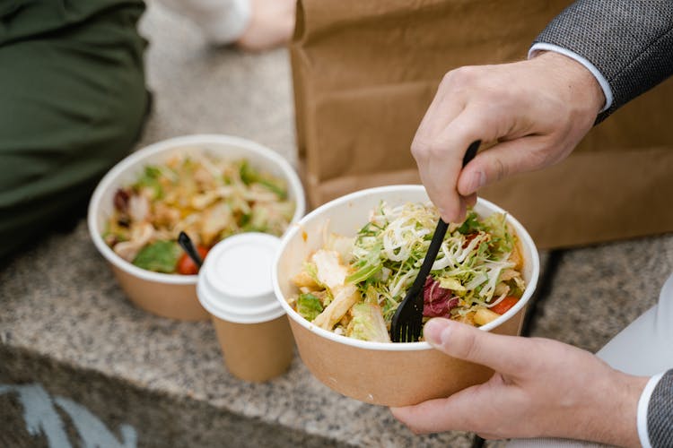 
A Close-Up Shot Of A Person Eating Food From A Takeaway Container