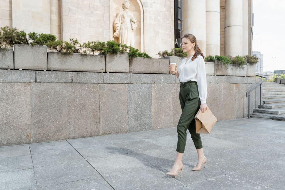 Professional woman walking outdoors in a polished summer work outfit with coffee and documents
