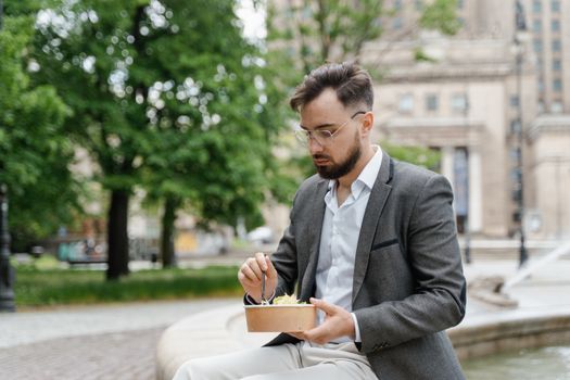 A businessman in a suit enjoys a takeaway lunch outdoors in a city park.