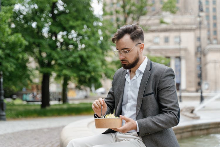 
A Bearded Man In A Suit Eating Takeaway Food