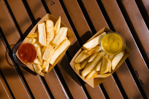 Free Two servings of crispy French fries with ketchup and mustard on a wooden table. Stock Photo