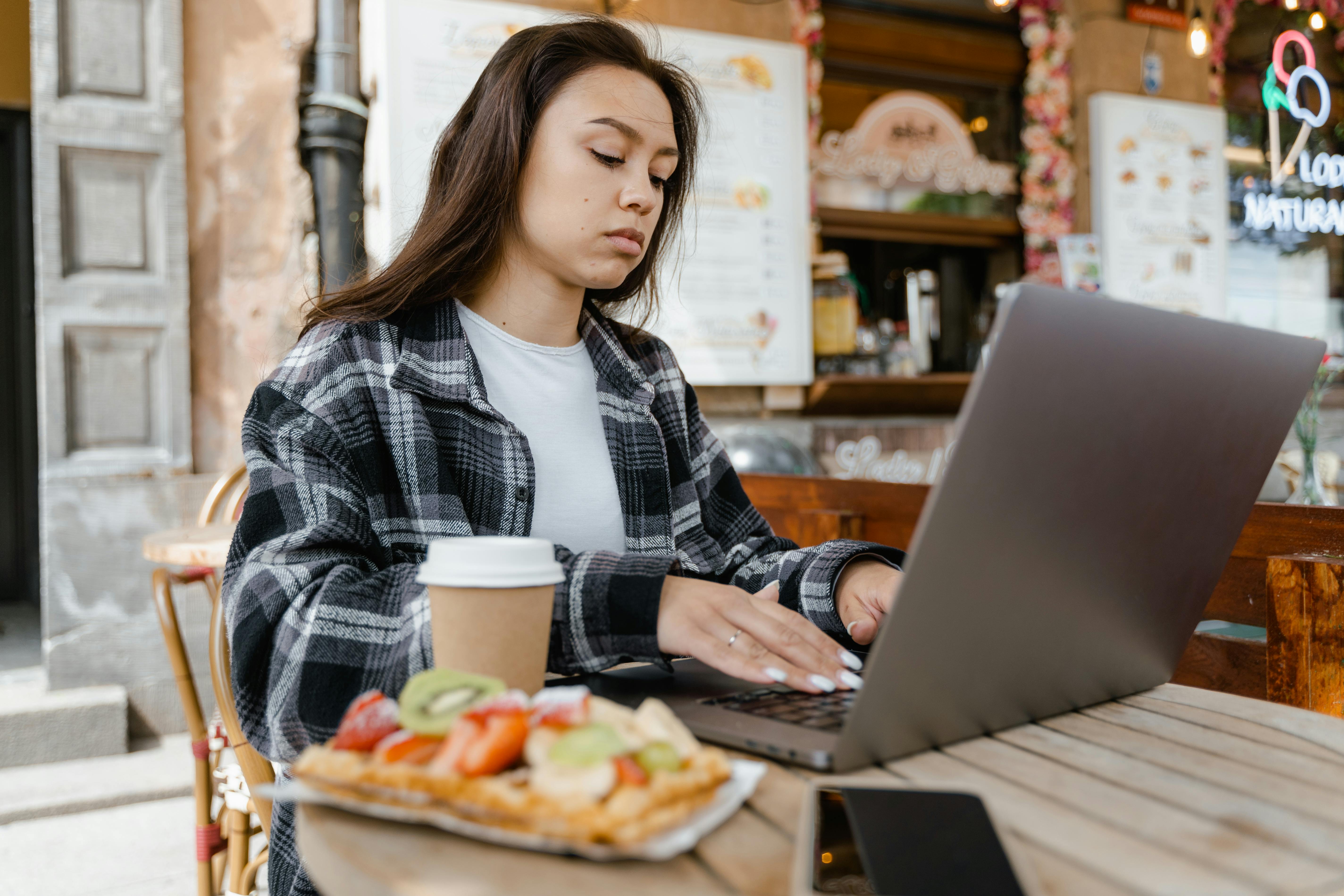 a woman wearing a plaid shirt typing on a laptop