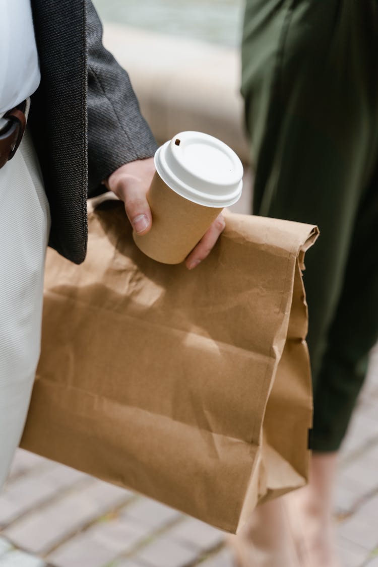 Person Holding A Food Takeaway Paper Bag And A Cup