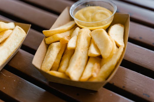 Close-up of delicious crispy French fries in a cardboard tray with mustard dip, ideal for snack or fast food concepts.