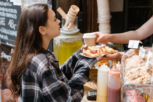 A young woman receives a delicious waffle and coffee at a street food stall.
