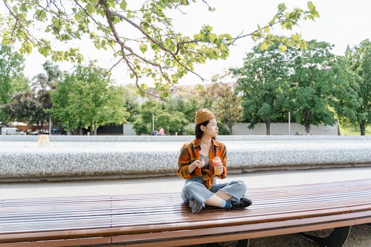 Woman Sitting On A Wooden Bench While Eating