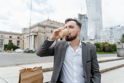 Free Young businessman in a suit enjoying coffee outdoors in a European city. Stock Photo