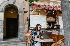 A woman at an outdoor cafe working on a laptop with coffee and snacks.