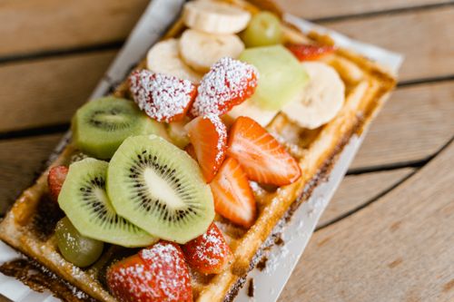 Free A delicious waffle topped with fresh fruits like kiwi and strawberries, served on a wooden table. Stock Photo