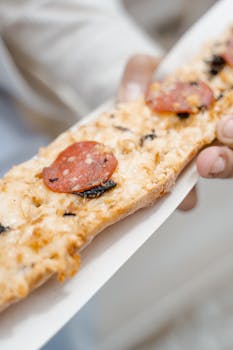 Delicious pepperoni flatbread held in hand, showcasing savory toppings. Ideal for food photography.