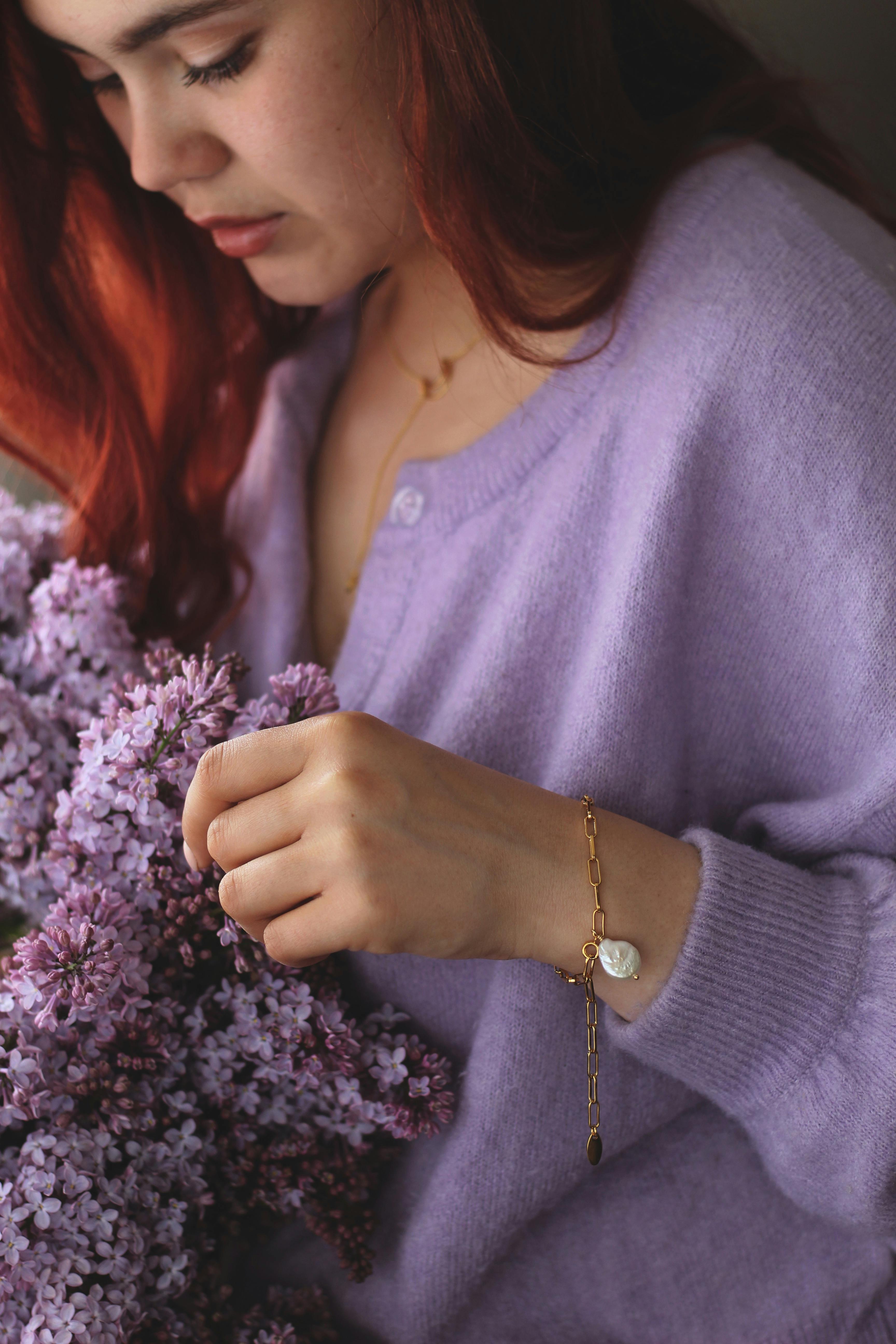 Beautiful woman in a purple sweater holds lilac flowers, showcasing gentle elegance.
