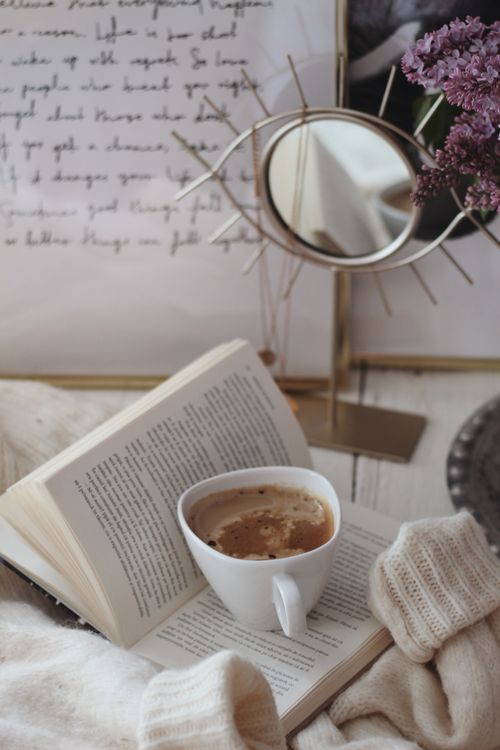Free A warm cup of coffee rests on an open book beside lilac flowers, creating a cozy reading nook. Stock Photo