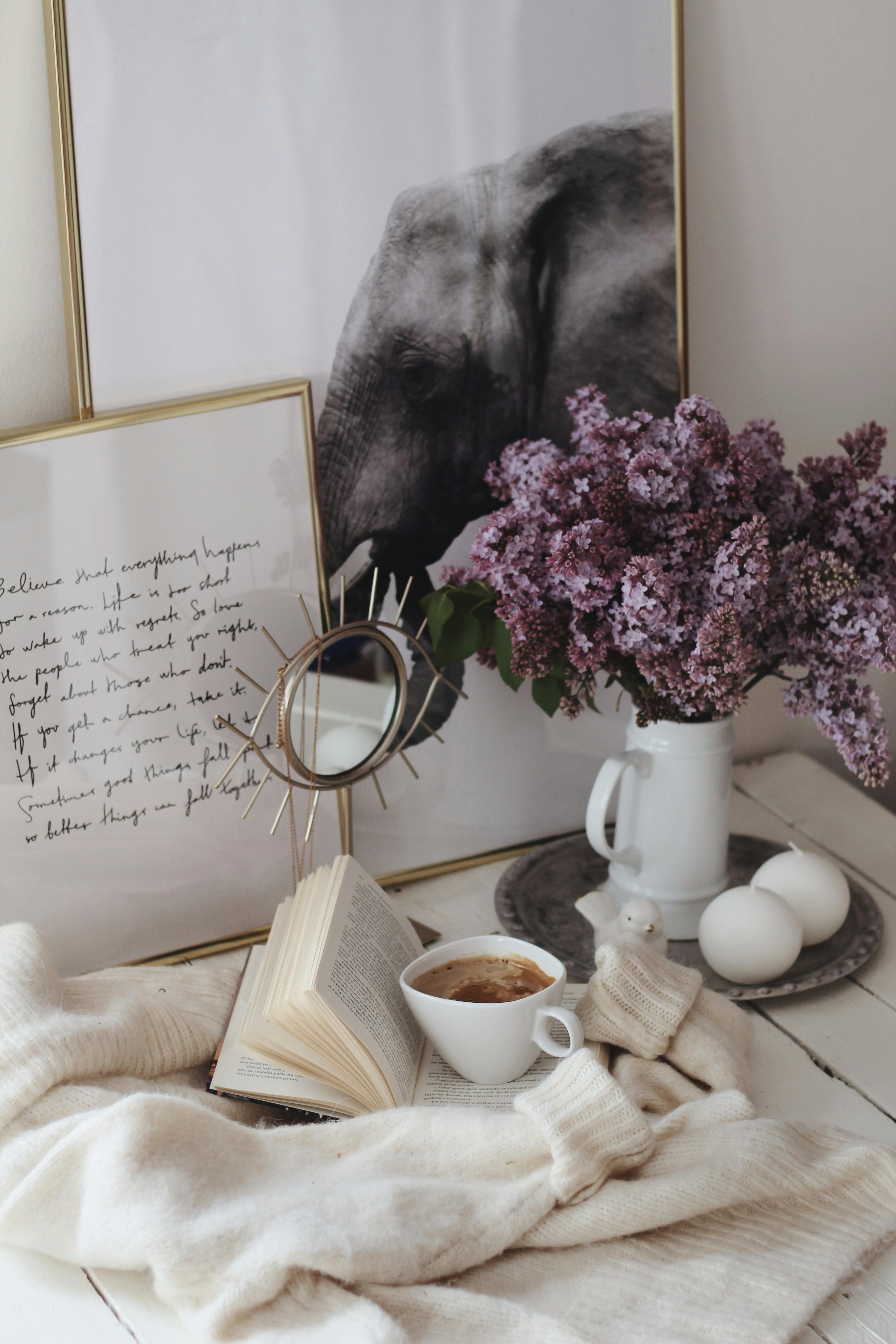 Aesthetic arrangement of coffee, lilacs, and art creating a cozy and artistic atmosphere.