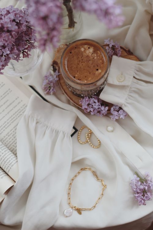 Free A cozy flat lay with lilacs, a cappuccino, and a white blouse, creating a serene morning vibe. Stock Photo