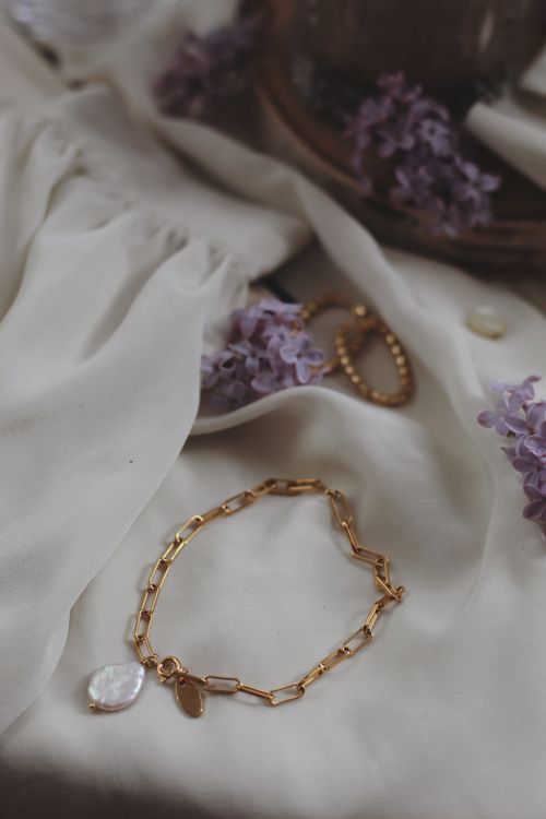 Free Close-up of gold bracelet and purple lilacs on white fabric, showcasing elegance and style. Stock Photo