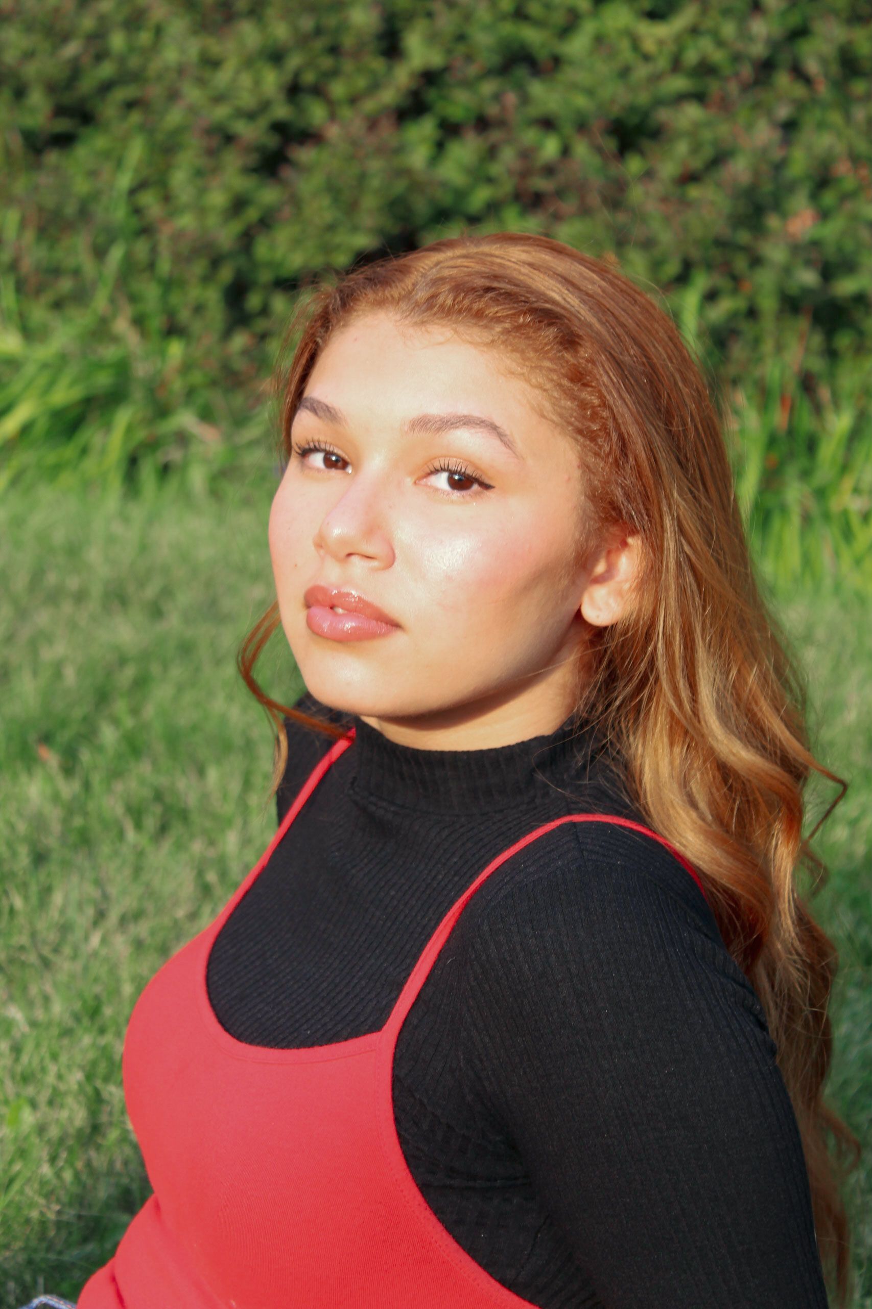 Portrait of a woman in red and black attire, sitting outdoors on a sunny day.