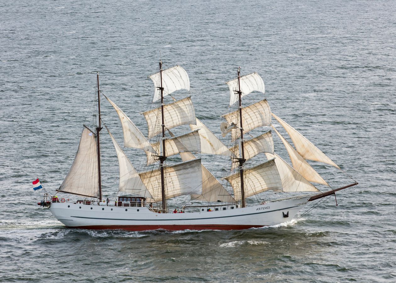 Majestic tall sailing ship with white and red sails crossing open blue sea water