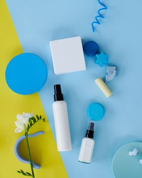 Flat lay of assorted spray bottles and geometric items on vibrant yellow and blue background.