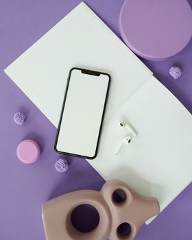 Minimalist flat lay of smartphone with earbuds and design elements on a purple surface.