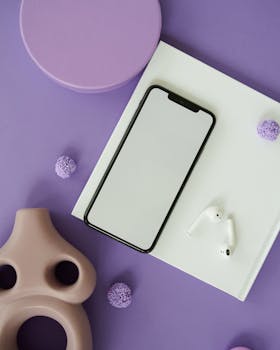 Top view of a smartphone and wireless earbuds arranged on a purple background for a modern tech flat lay.