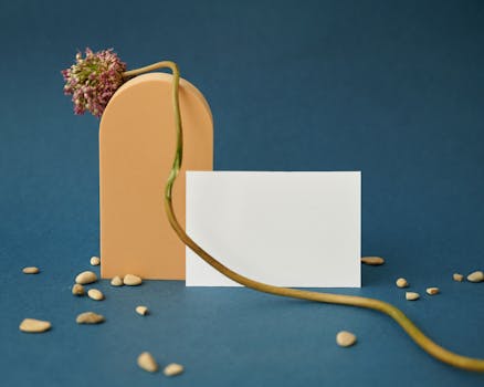 Elegant mockup display with a flower, card, and pebbles on a blue surface, perfect for design presentations.