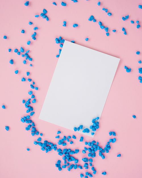 Free Flat lay of a white paper on a pink surface with scattered blue pebbles. Stock Photo