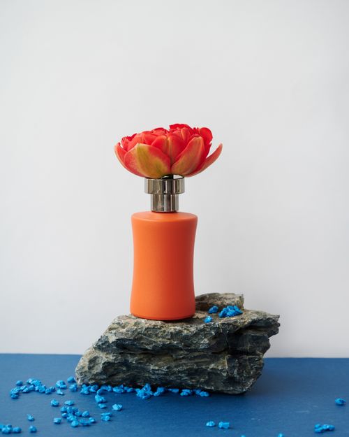 Free Orange perfume bottle with a vibrant tulip cap atop rocks with blue decorative elements. Stock Photo