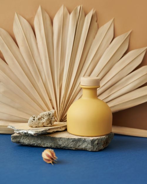 Free A minimalist setup of a yellow bottle with dried palm leaves and stones. Stock Photo