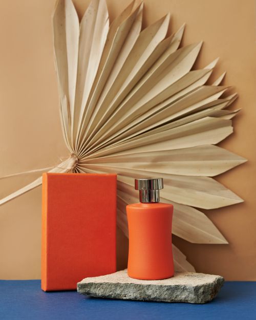 Free Stylish product shot featuring an orange perfume bottle with dried palm leaves in a minimalist setting. Stock Photo