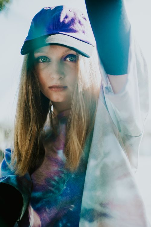 Free Portrait of a young woman wearing a tie-dye shirt and cap, looking thoughtfully at the camera. Stock Photo