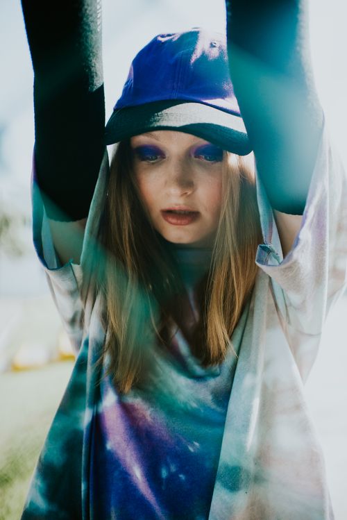 Free Stylish woman wearing a cap and tie-dye shirt, captured in vibrant sunlight. Stock Photo