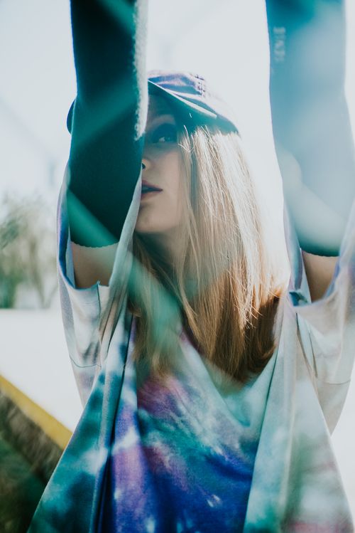 Free Stylish young woman wearing tie dye shirt poses in urban sunlight, showcasing modern street fashion. Stock Photo