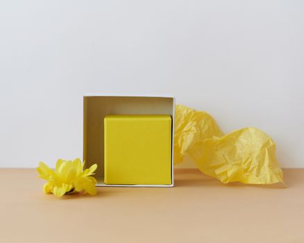 Minimalist composition with a yellow gift box, flower, and tissue paper.