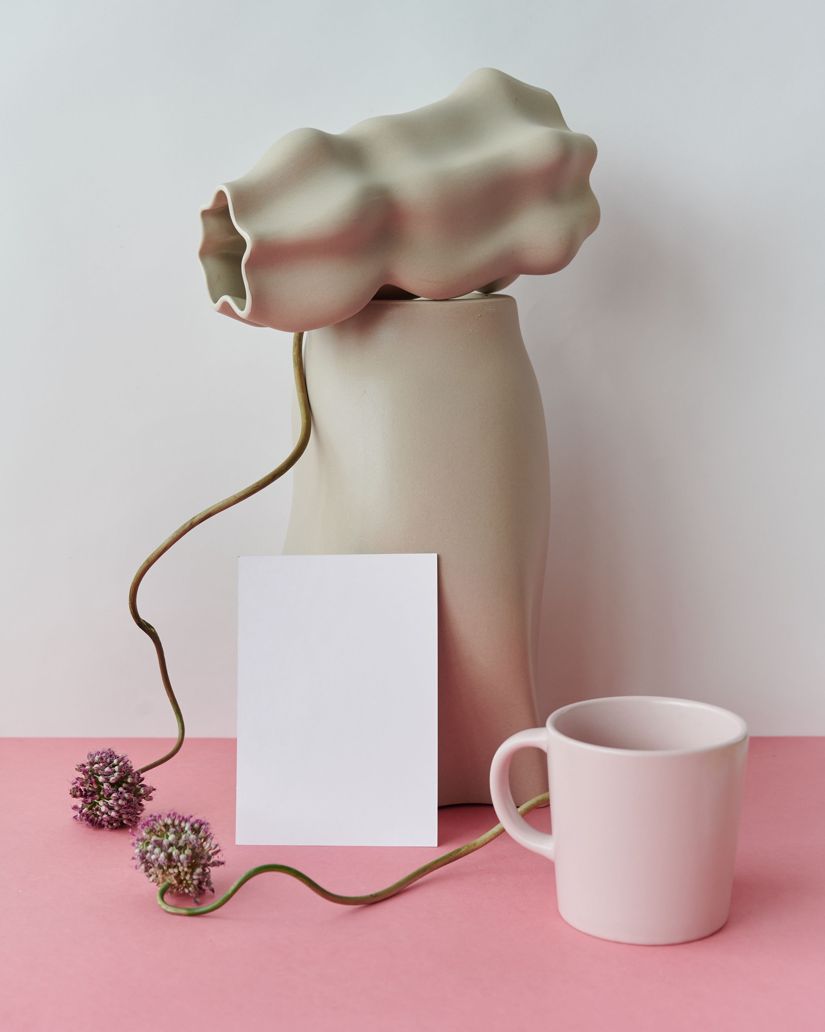 Modern minimalist arrangement featuring a vase, mug, and flowers on a pink surface.