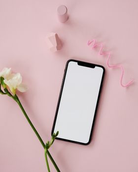 Flat lay of smartphone with pink background and flower offering copy space for creatives.