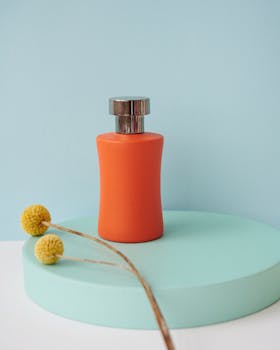 Orange perfume bottle displayed on a pastel platform with a flower accent.