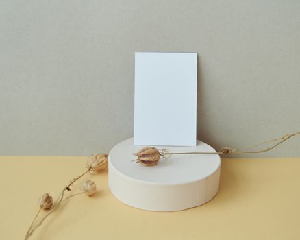 A simple mockup with dried flowers and a blank card on a cylindrical platform.