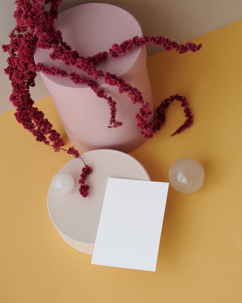 Free A minimalist still life featuring pink artificial amaranth, glass spheres, and blank card on a vibrant yellow backdrop. Stock Photo