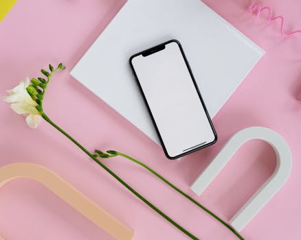 Flat lay of a smartphone mockup on a pastel background with a freesia flower and geometric shapes.