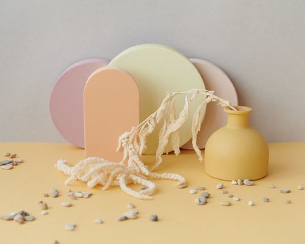 A minimalist still life featuring dried flowers in a pastel vase with scattered pebbles.