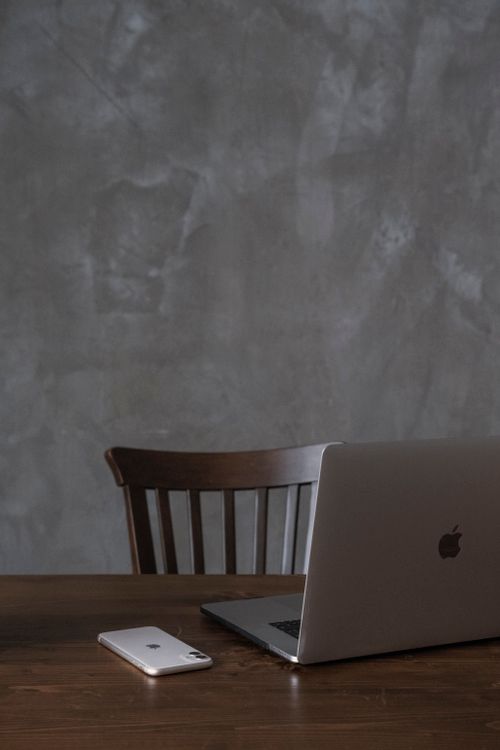 Free Modern gray open netbook and phone placed on wooden table near wooden chair against gray wall in light apartment Stock Photo
