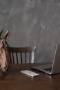 Gray portable computer and telephone placed on wooden desk near horse bust figurine against gray background