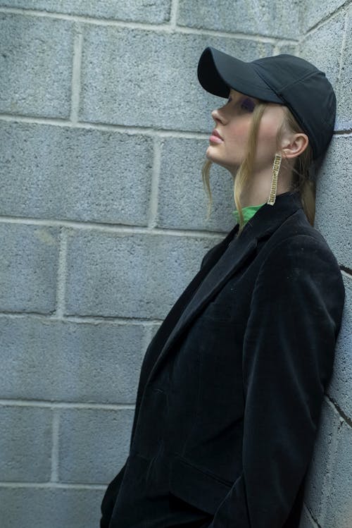 A Woman Wearing a Cap and a Black Jacket Leaning on a Wall