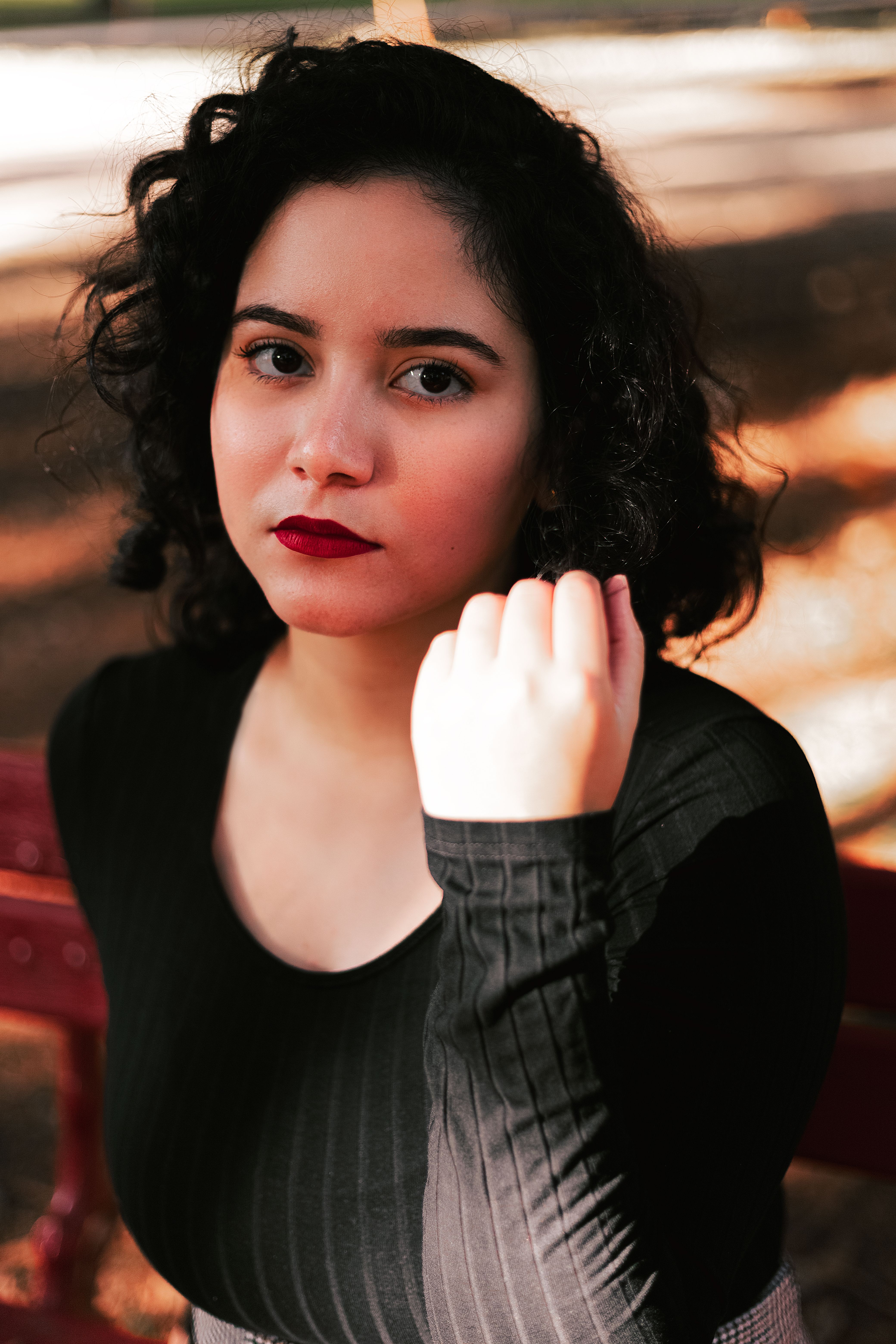 Indoor portrait of a woman with curly hair, wearing a black shirt and red lipstick.