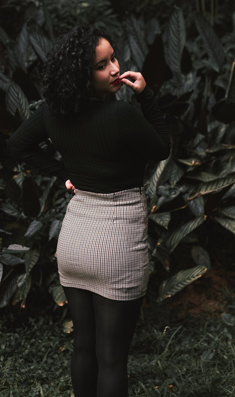 Woman In Black Long Sleeve And White Skirt Standing Near Green Plants