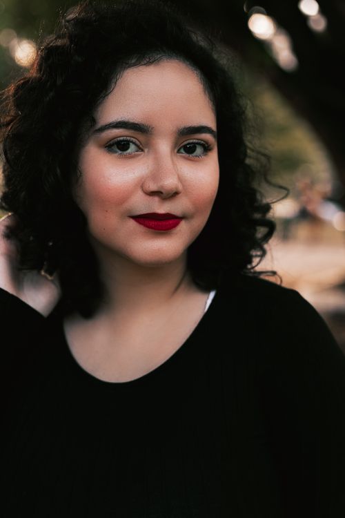 Free Portrait of a young woman with curly hair and red lipstick in a natural outdoor setting. Stock Photo